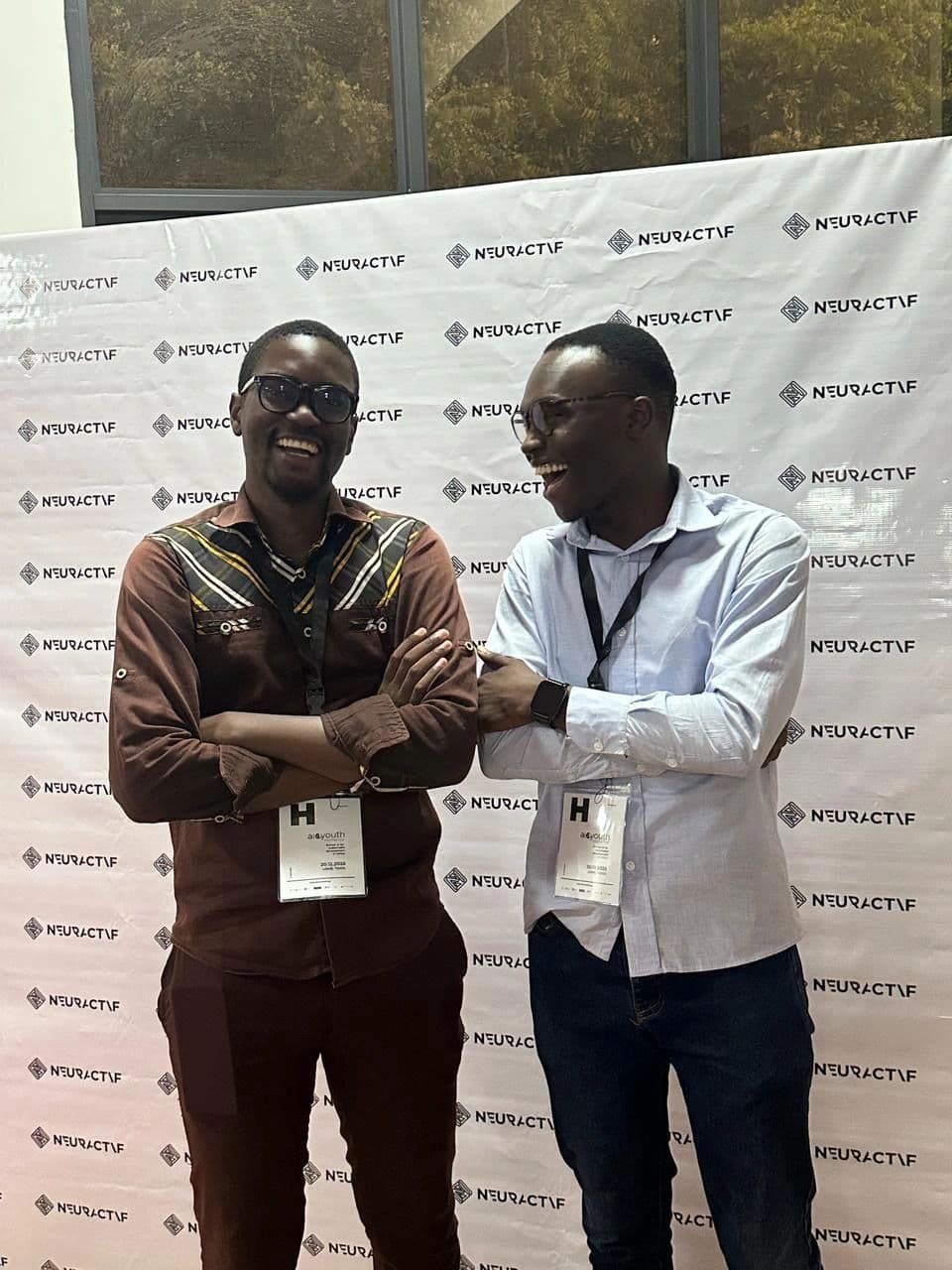 Ewan Semadegbe and Eli Jean Doumeyan laughing together in front of the Neuractif press wall.